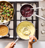 Thanksgiving side dishes cooking on Wolf gas stovetop including mashed potatoes, cranberry sauce, gravy, and roasted Brussels sprouts