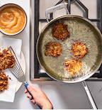 Potato latkes frying in Misen stainless steel pan with applesauce on the side