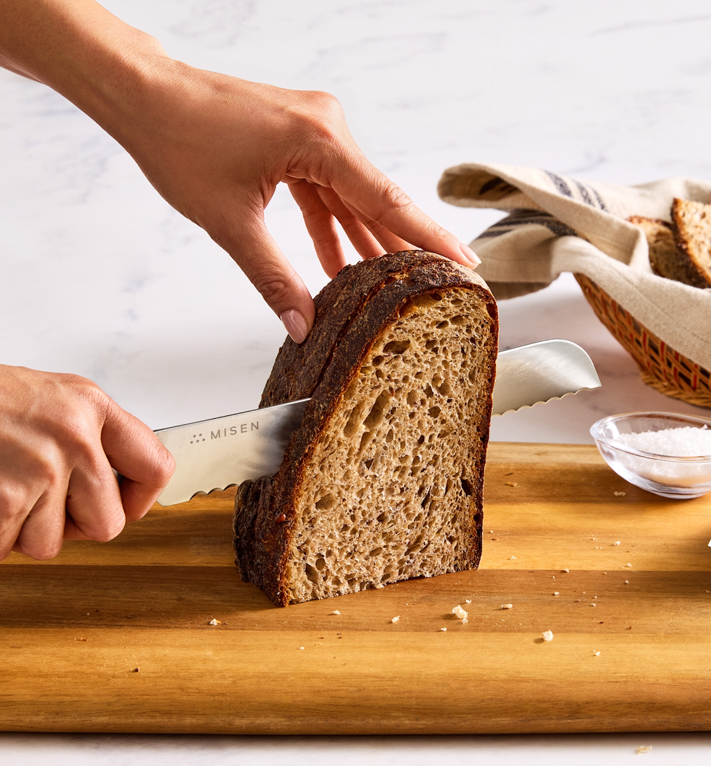 Misen serrated bread knife slicing dark sourdough loaf on wooden cutting board