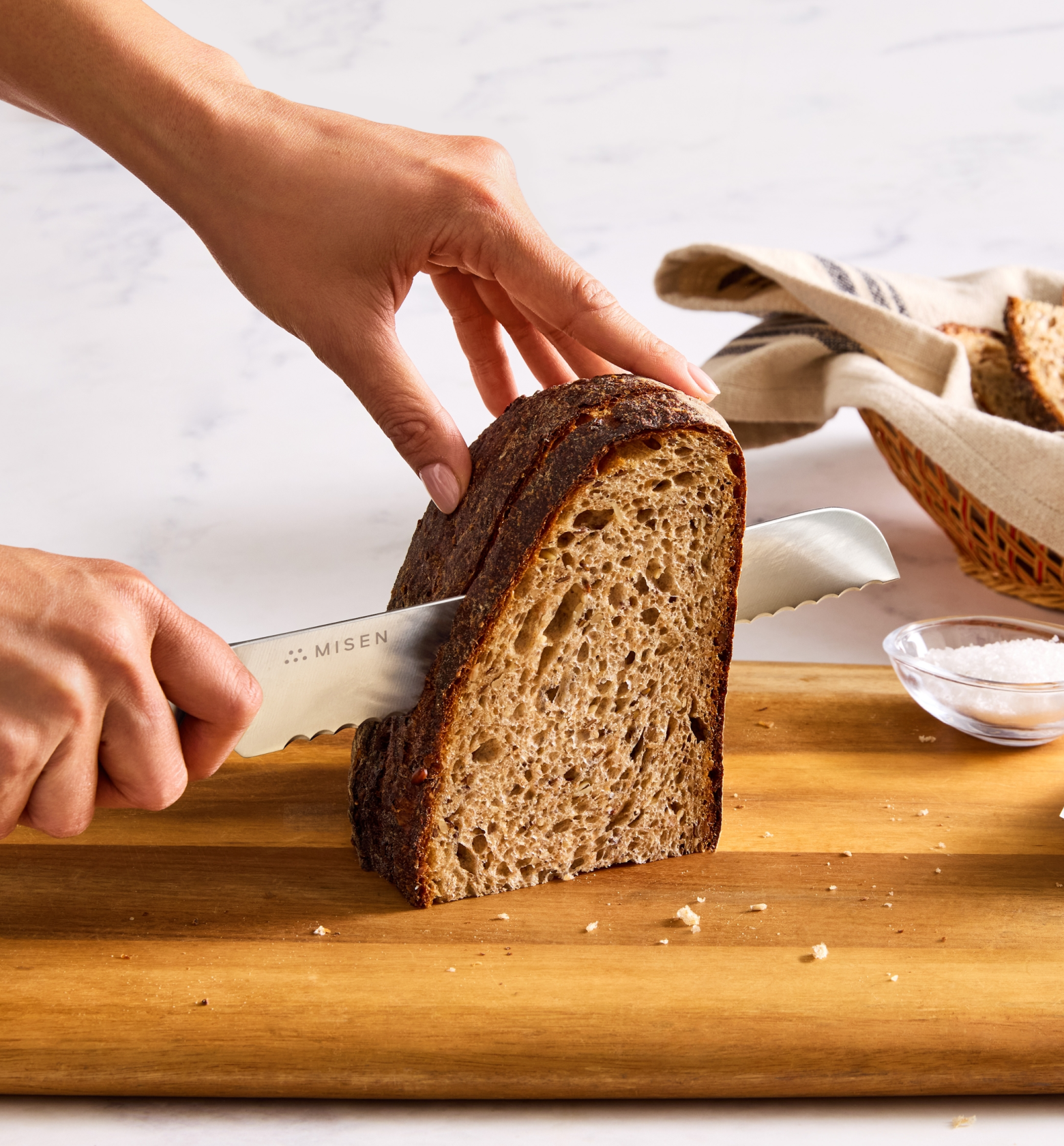 Misen serrated bread knife slicing dark sourdough loaf on wooden cutting board