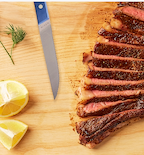 Sliced ribeye steak on wooden cutting board with Misen steak knife and lemon wedges