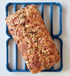 Homemade cranberry seed loaf bread topped with pumpkin seeds on blue cooling rack