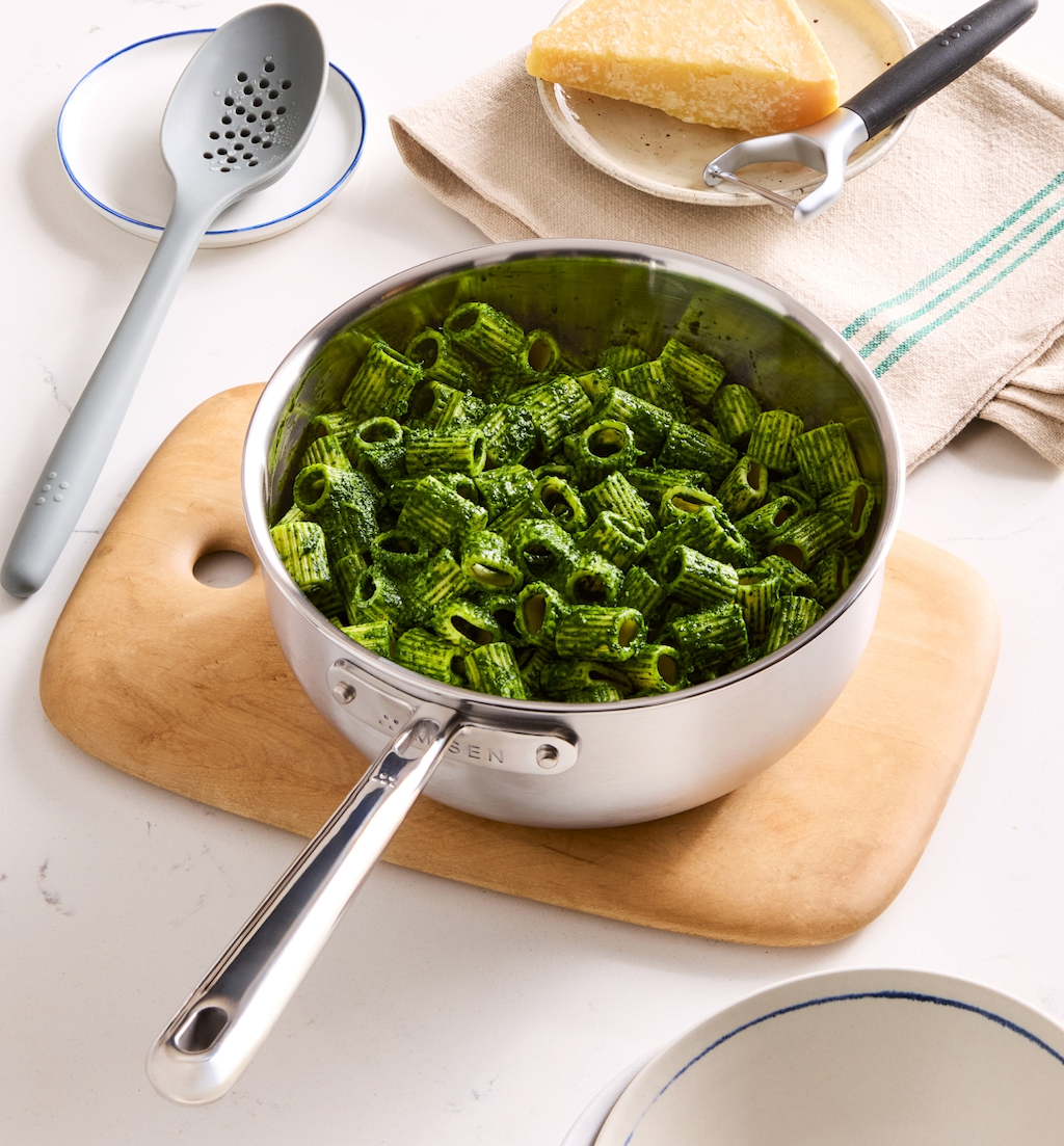 Rigatoni pasta with green pesto sauce in stainless steel sauté pan with Parmesan cheese