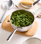 Rigatoni pasta with green pesto sauce in stainless steel sauté pan with Parmesan cheese