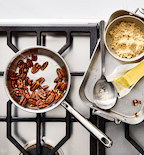 Misen stainless steel cookware with toasted pecans, brown sugar, butter, and measuring spoon on gas stovetop