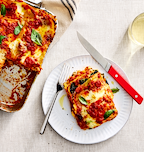 Homemade vegetarian lasagna slice on white plate with tomato sauce, melted mozzarella, and fresh basil