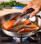 Pan-seared salmon fillets cooking in stainless steel skillet over gas flame