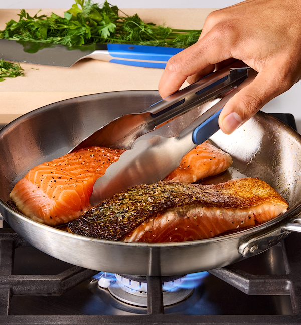 Pan-seared salmon fillets cooking in stainless steel skillet over gas flame