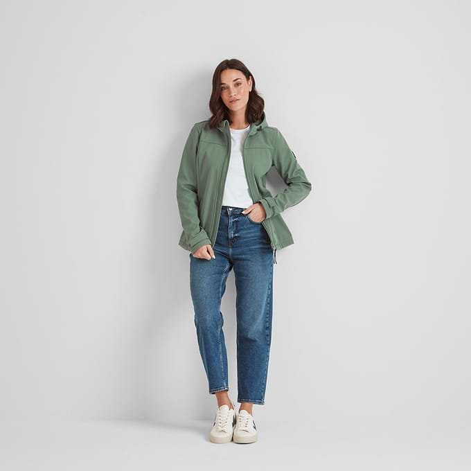 A woman modeling a hooded softshell jacket in light forest green color, paired with blue jeans and white shoes.