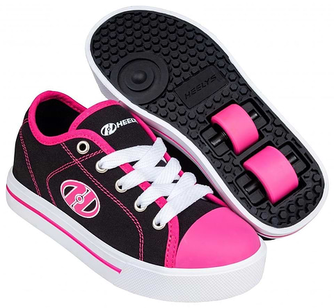 A pair of Heelys Classic X2 Shoes in black, white, and hot pink, featuring white laces. One shoe is upright with the Heelys logo and a pink toe cap, while the other is turned over to display two retractable wheels on the sole.