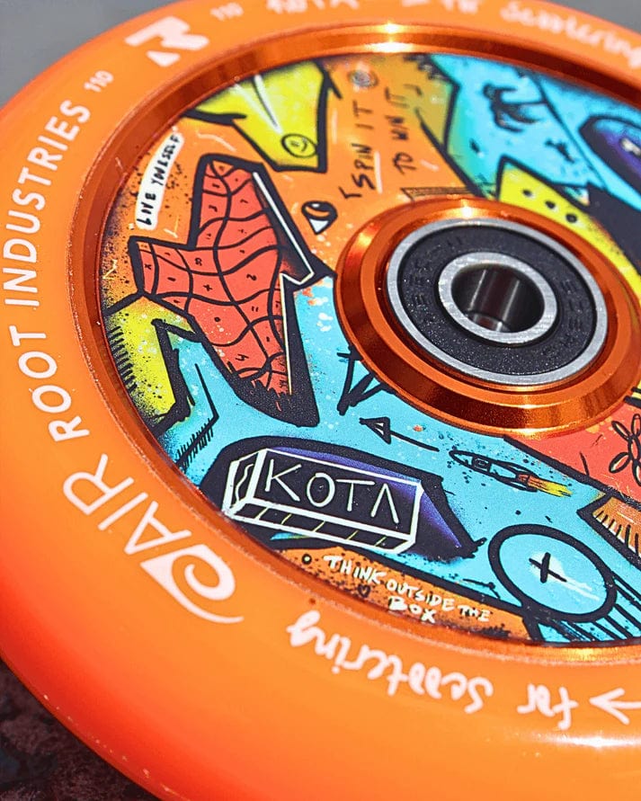 Close-up of the orange Root Industries x KOTA Limited Edition AIR 110mm Stunt Scooter Wheel, featuring a graffiti-style inner circle with abstract shapes, doodles, and "KOTA" prominently displayed.