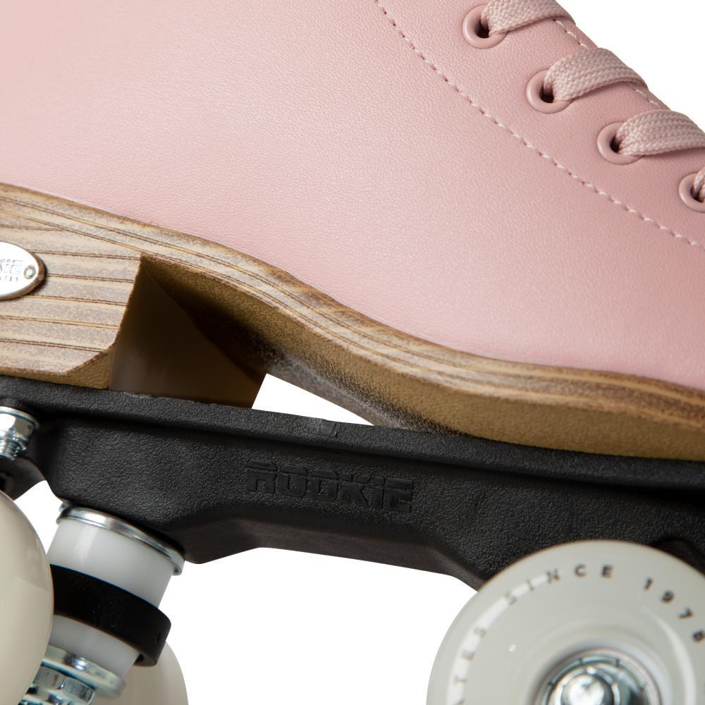 Close-up of the Rookie Classic 78 Quad Roller Skates - Pink by Rookie, featuring a pink boot, light wood sole, white wheels, and a black skate plate embossed with "Rookie" for a classic look and premium detail.