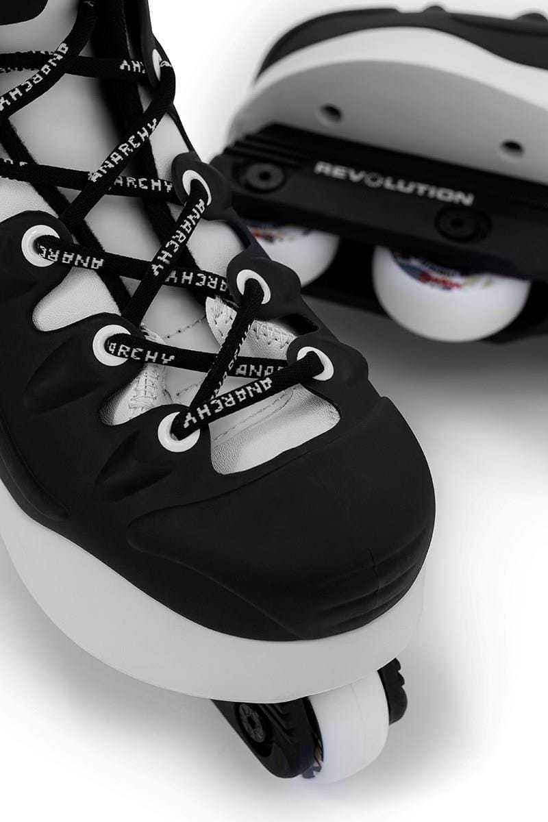 Close-up of Anarchy Revolution II black aggressive inline skates, showcasing white laces and wheels. Designed for performance and durability, "REVOLUTION" appears on the blade frame with the brand name Anarchy repeatedly featured on the laces.