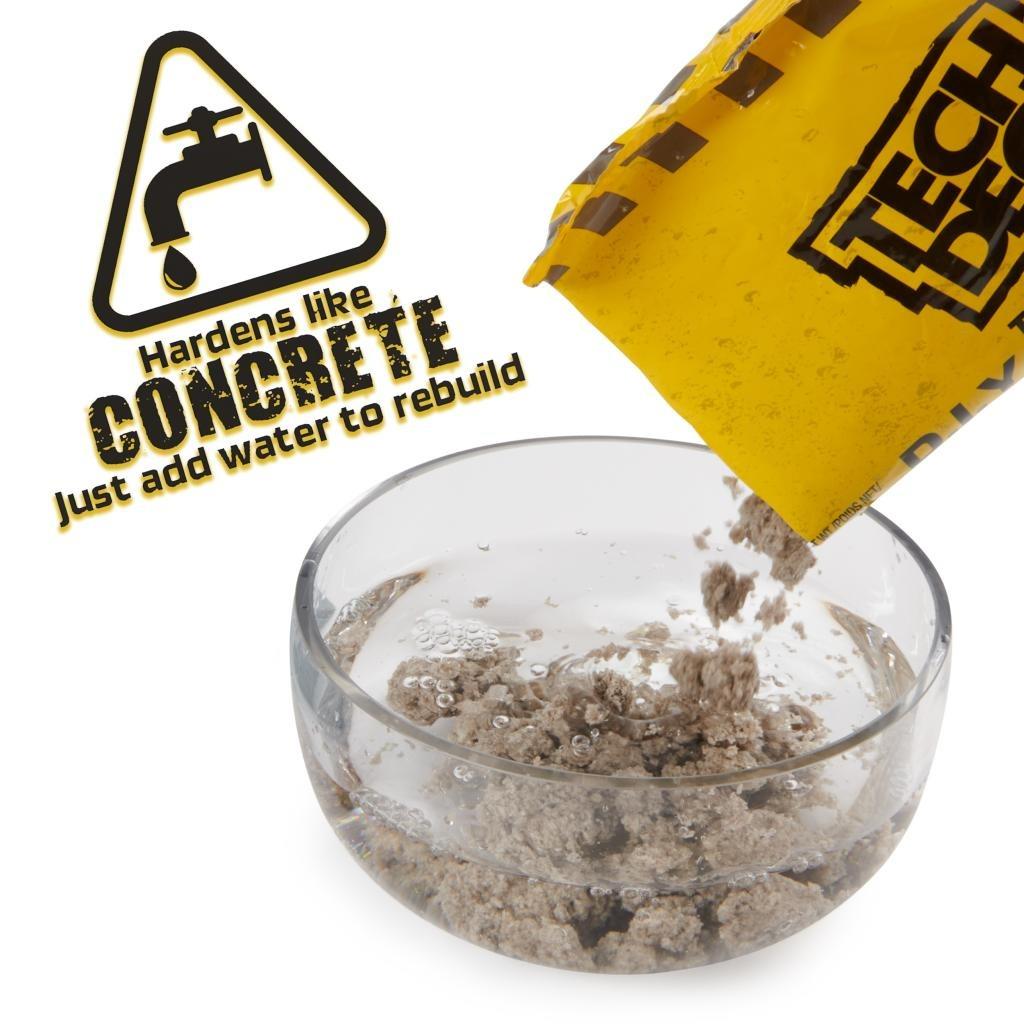A hand pours gray powder from a yellow Tech Deck DIY Concrete Reusable Fingerboard Ramp Modelling Set packet into water. A warning shows: “Hardens like CONCRETE. Just add water to rebuild.” Create custom ramps for your Tech Deck fingerboard!.