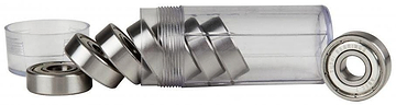 A transparent cylindrical container, open with several Sushi Chrome ABEC 7 Skateboard Bearings, spills some while others remain. Additional precision bearings are visible beside it, and the separated cap lies nearby.