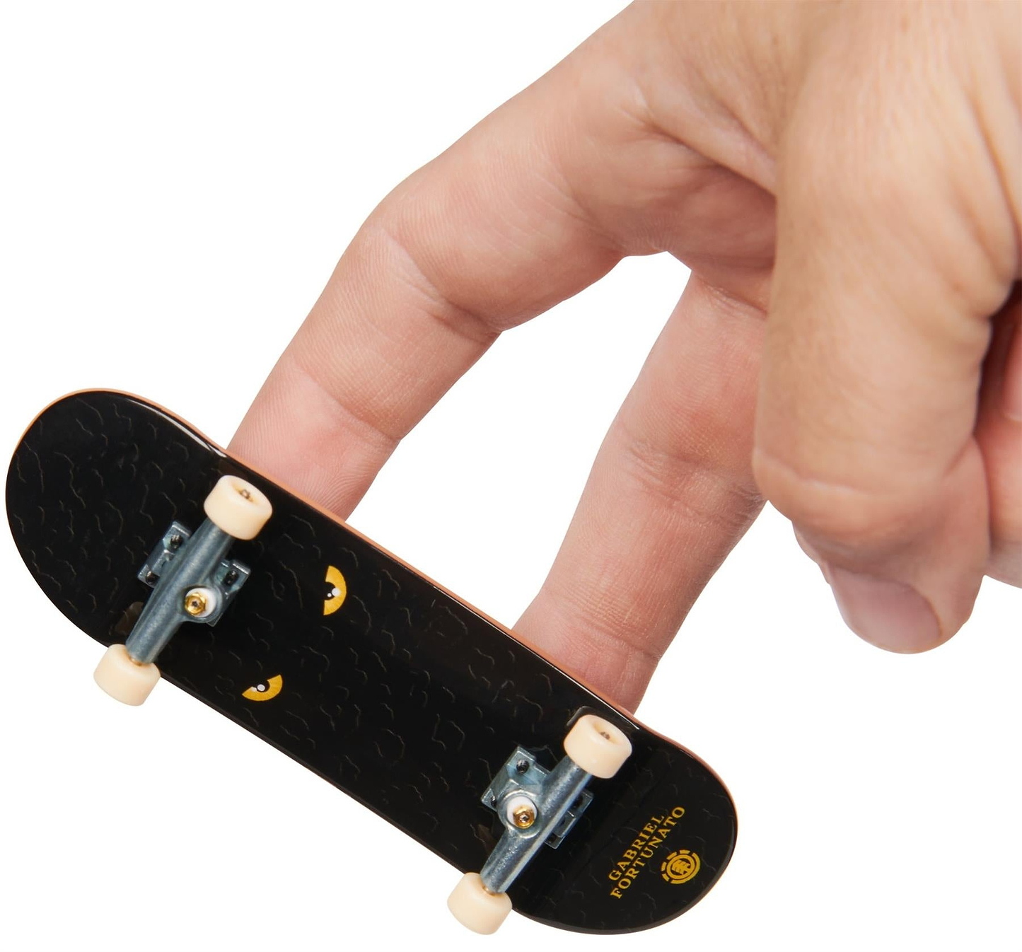 A hand uses two fingers to ride a Tech Deck M01 Deluxe 4 Pack Fingerboards - Element mini skateboard against a white background.