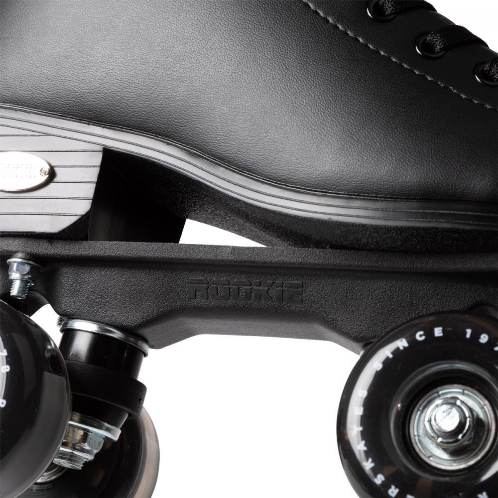 Close-up of the Rookie Classic 78 Quad Roller Skates - Black by Rookie, featuring part of the boot, metal plate, and two black wheels with white text. Laces and textured detailing showcase their classic style.