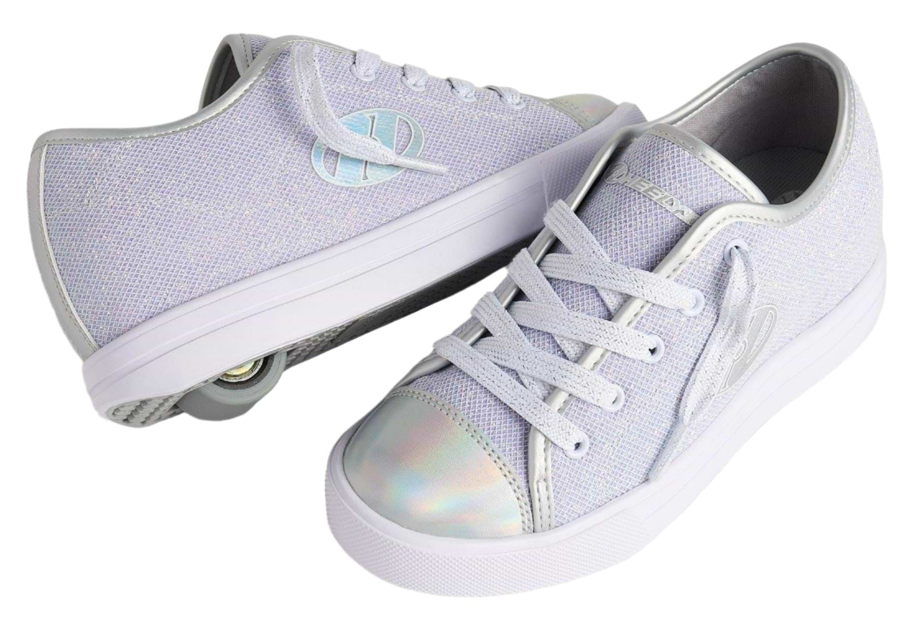 A pair of Heelys Classic Em Girls Shoes in Silver/White/Grey with a mesh upper, white laces, and iridescent toe caps. One shoe displays the brand’s signature retractable heel wheel with ABEC 3 bearings; the other rests on its side.