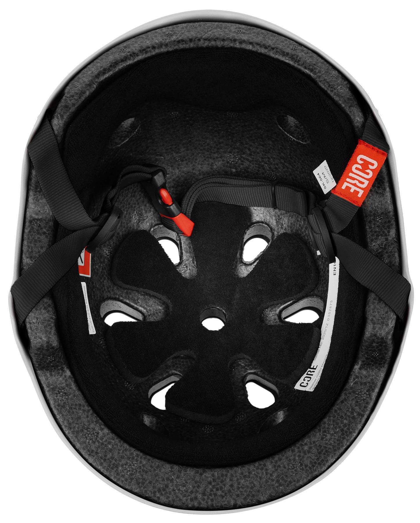The image shows the interior of the CORE Street Skate / Scooter Helmet - White by CORE, featuring foam padding, ventilation holes, black straps, a red buckle, and tags with "CORE" printed on them.