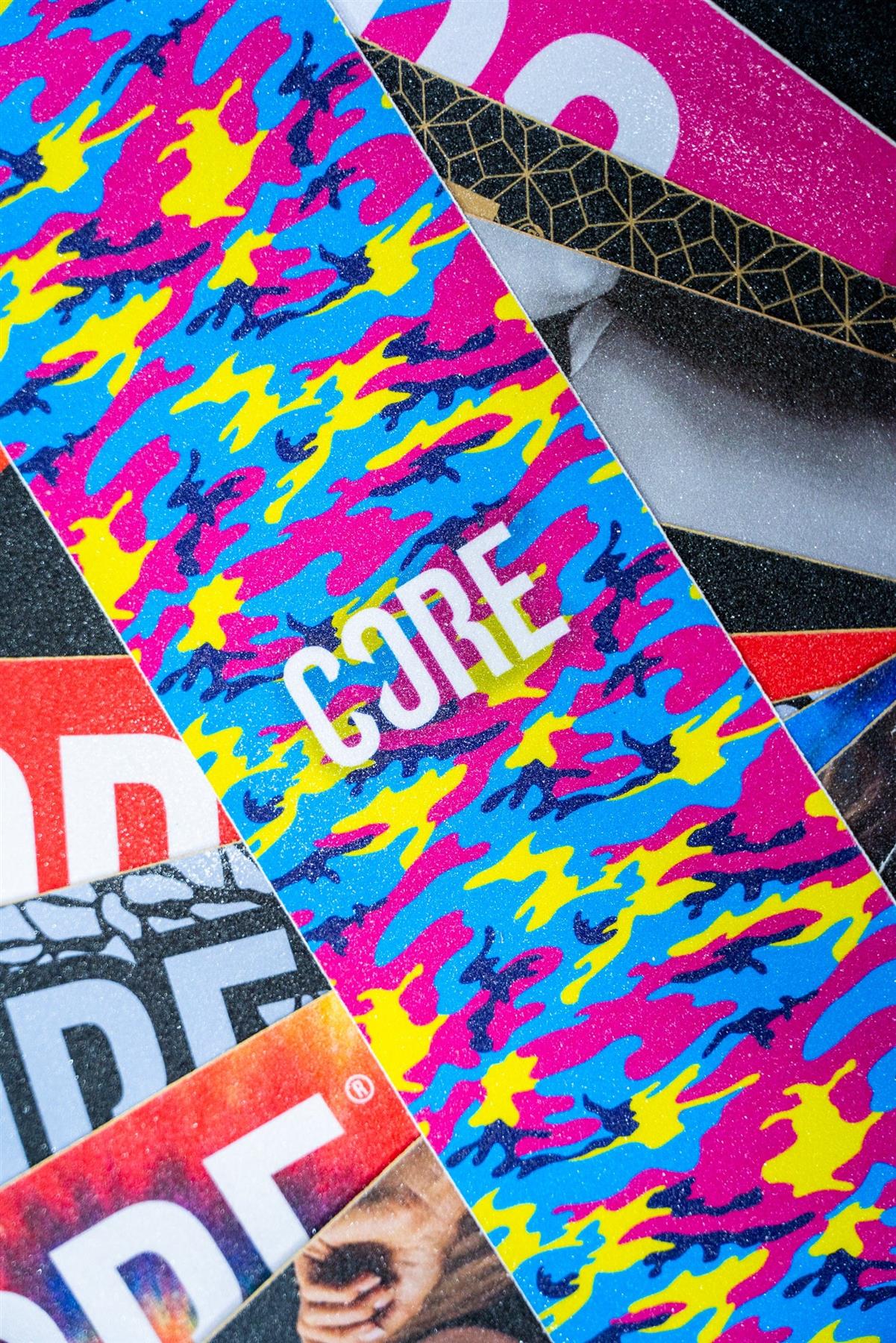 The CORE Stunt Scooter Griptape - Neon Camo features vibrant blue, pink, and yellow camouflage with "CORE" in bold white letters—ideal grip tape for customizing your stunt scooter.
