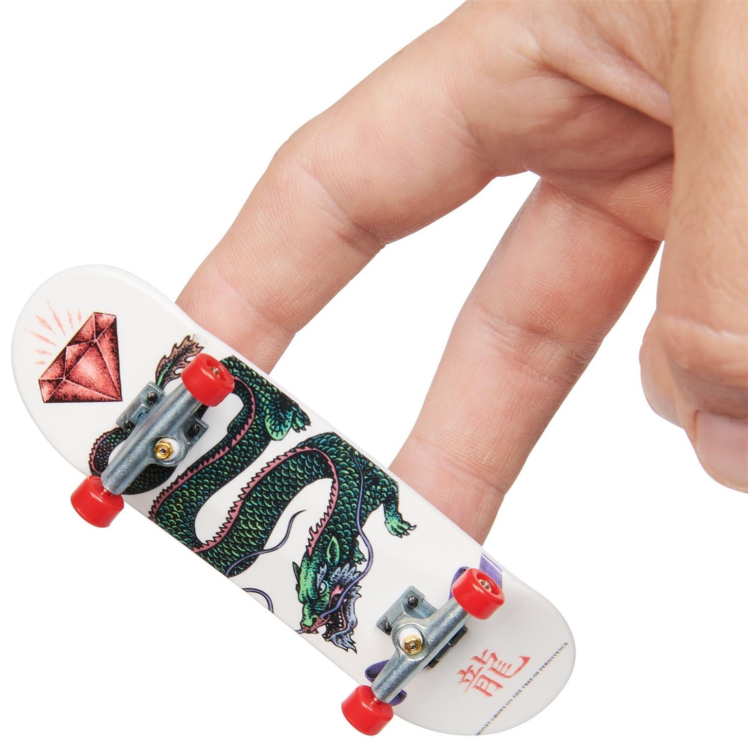 A hand uses two fingers to maneuver a Tech Deck M01 Deluxe 4 Pack Fingerboard - Diamond featuring authentic skateboard graphics—a green dragon, red diamond, and Chinese characters. The perfect addition to any Tech Deck collection.