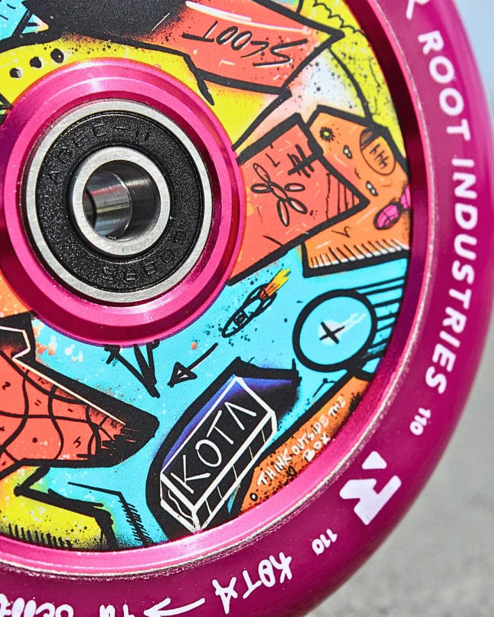 Close-up of the Root Industries x KOTA Limited Edition AIR 110mm Stunt Scooter Wheel in purple, featuring a pink rim, bold graffiti-style art, and "KOTA" branding.