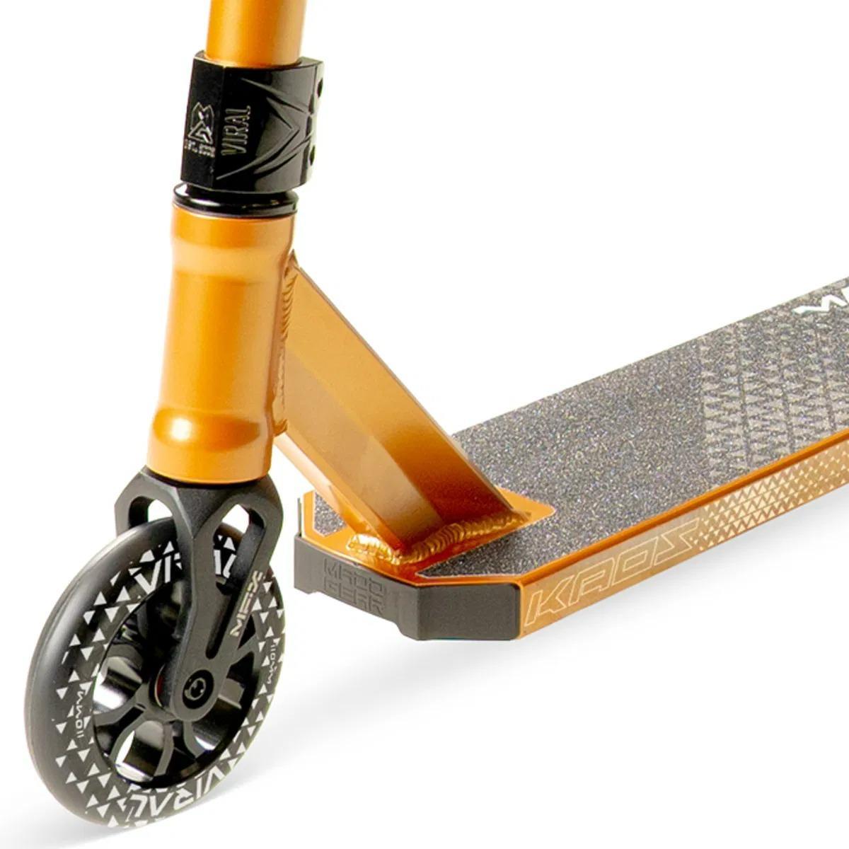 Close-up of the Madd Gear Viral KAOS Complete Stunt Scooter - Copper, highlighting its copper and black deck with grip tape, distinctive front wheel with white graphics, and part of the handlebar stem.