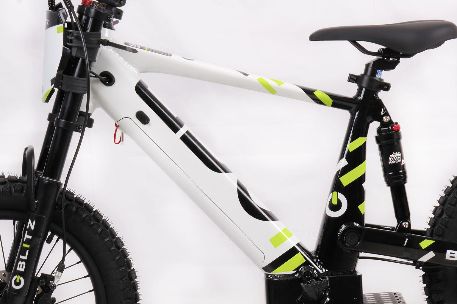 Side view of the Duo 18" Blitz Kids Electric Balance Bike by Duo in white and black with neon yellow stripes, thick tires, front suspension fork, and rear shock absorber, set against a plain white background.