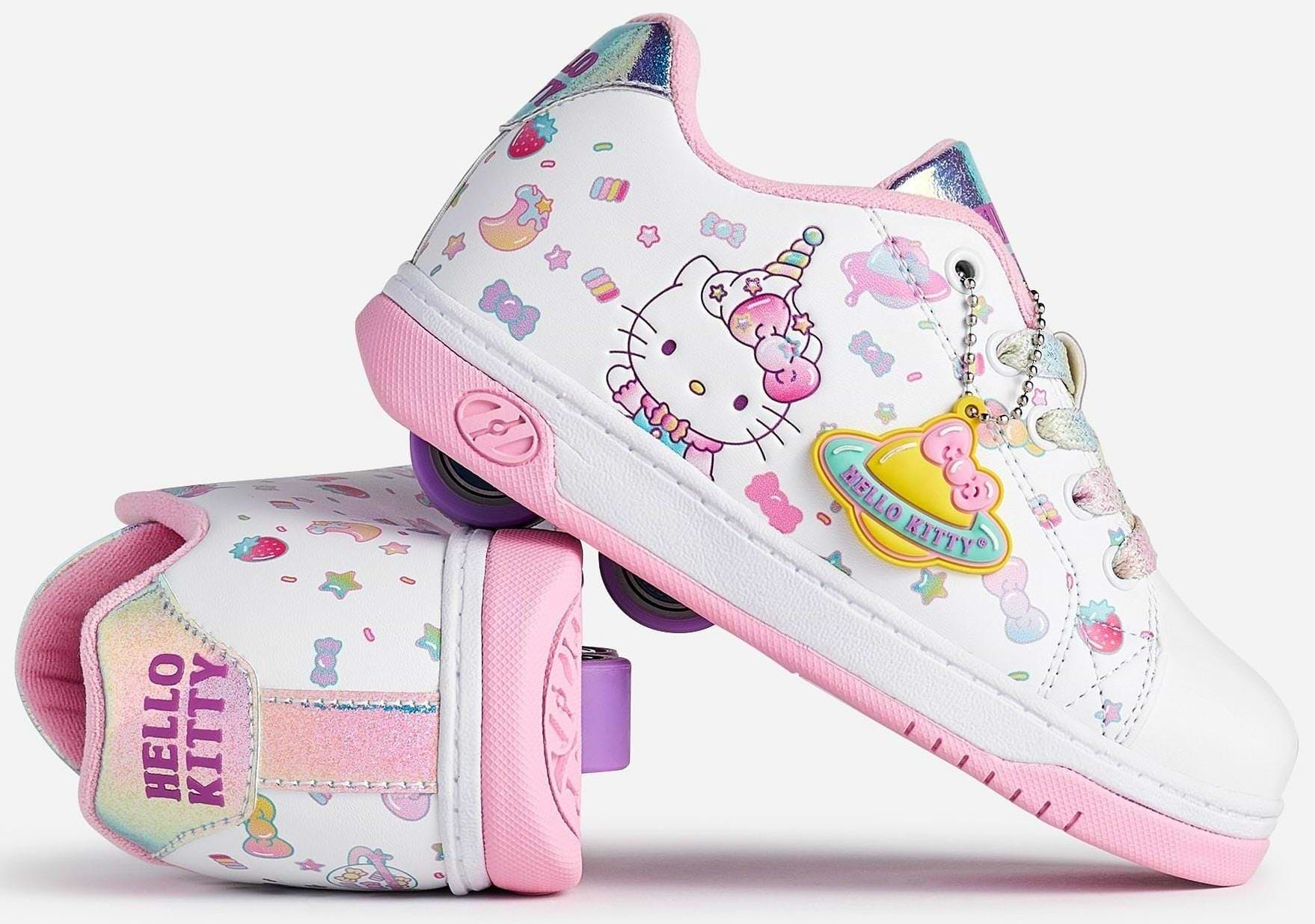 Two Heelys x Hello Kitty Split X2 Girls Heelys in white and pink, featuring unicorn, rainbow, star, and heart designs. One shoe is upright; the other is on its side, displaying "HELLO KITTY" text and a colorful planet charm. Brand: Heelys.