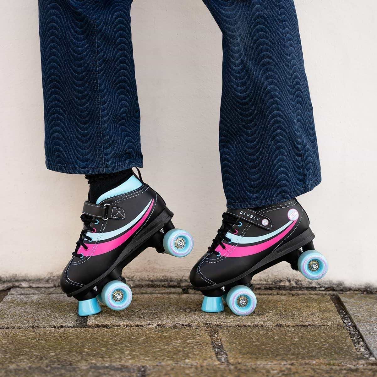 A person stands on stone pavement wearing Osprey Disco Quad Roller Skates - Black by Osprey, with only their lower legs and blue textured pants visible—ideal for indoor and outdoor skating fun.