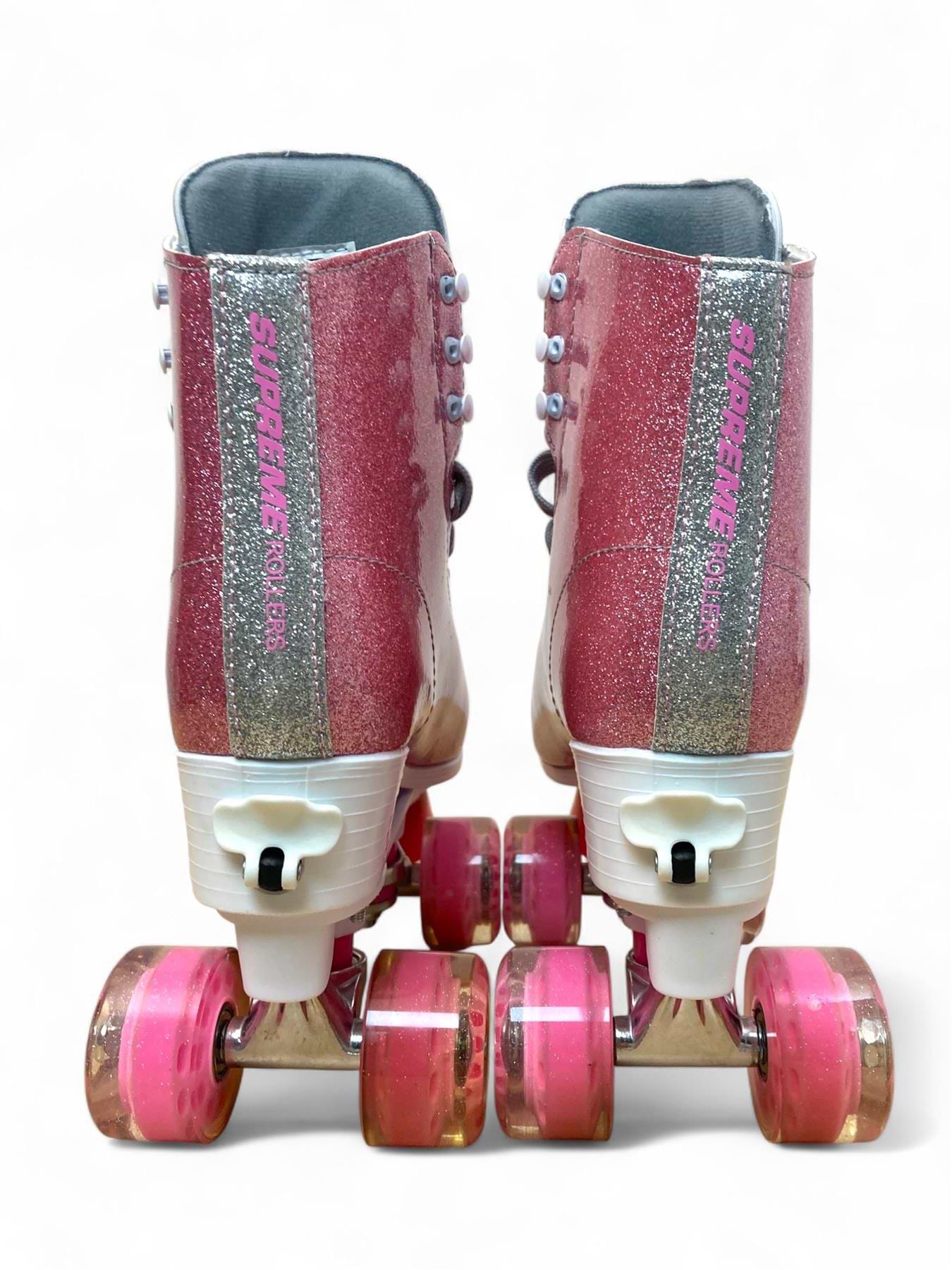 The Supreme Del Rey Adjustable Quad Roller Skates - Pink by Supreme feature pink glitter, white laces, and pink wheels—viewed from behind on a white background—ideal kids' outdoor roller skates for fun adventures.