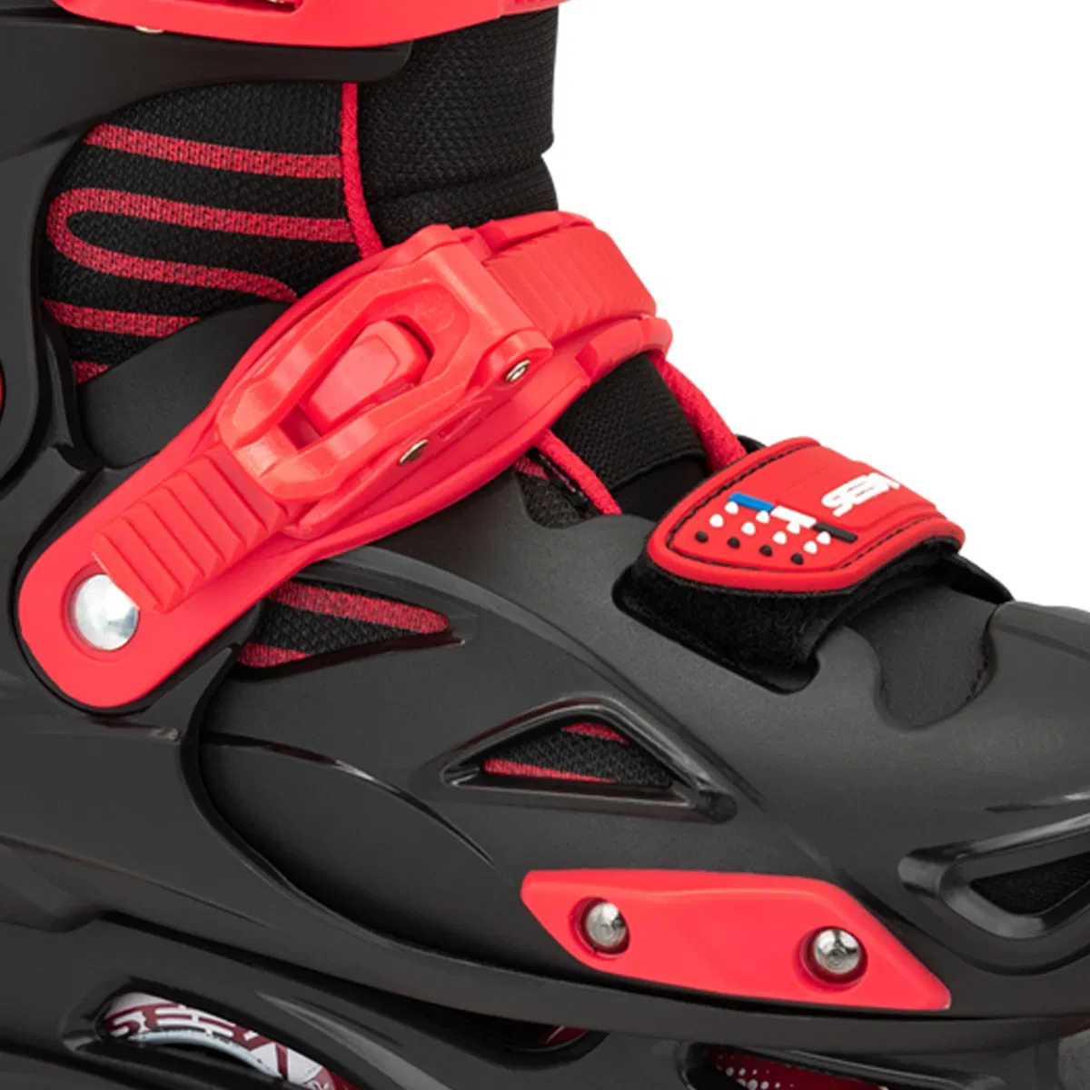 Close-up of Seba STJ Junior Adjustable Inline Skates in black and red, featuring a red buckle strap, black mesh with red accents, and a stars-and-stripes patch. Ideal for beginners; partial view of wheel and frame at the bottom.