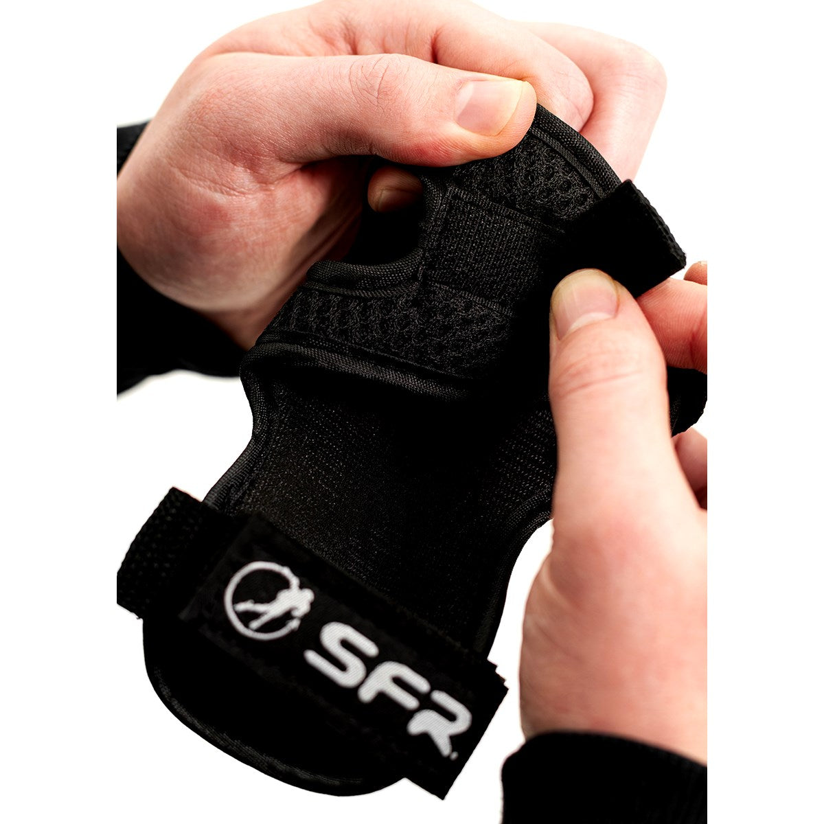 A person adjusts a black SFR wrist guard with a Velcro strap, designed for sports protection—perfect to pair with the SFR Essentials Youth Triple Pad Set V2 - Black.