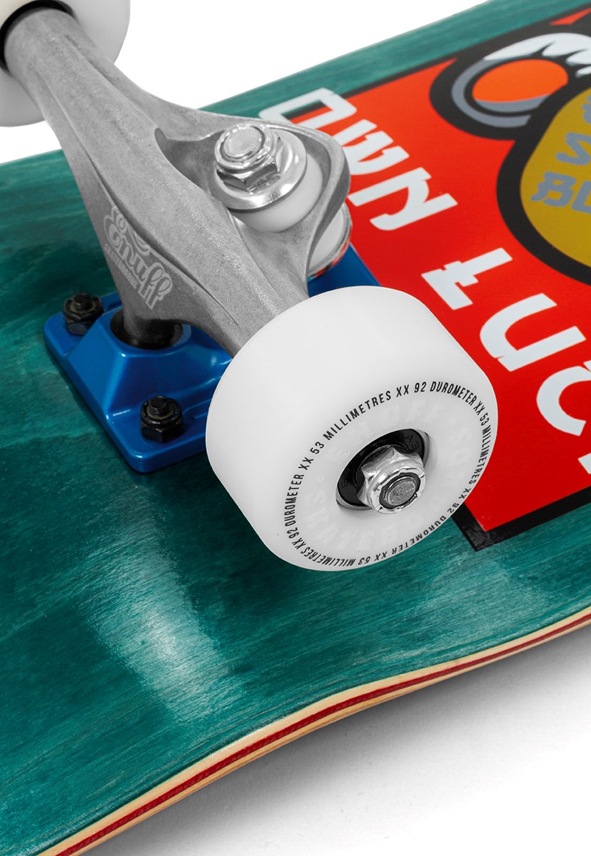 Close-up of an Enuff Lucky Cat Green Complete Skateboard (8″ x 32″) wheel and truck mounted on a teal deck featuring a colorful graphic and visible text. The white wheel with black writing is perfect for beginner skateboarders interested in street and park skating.