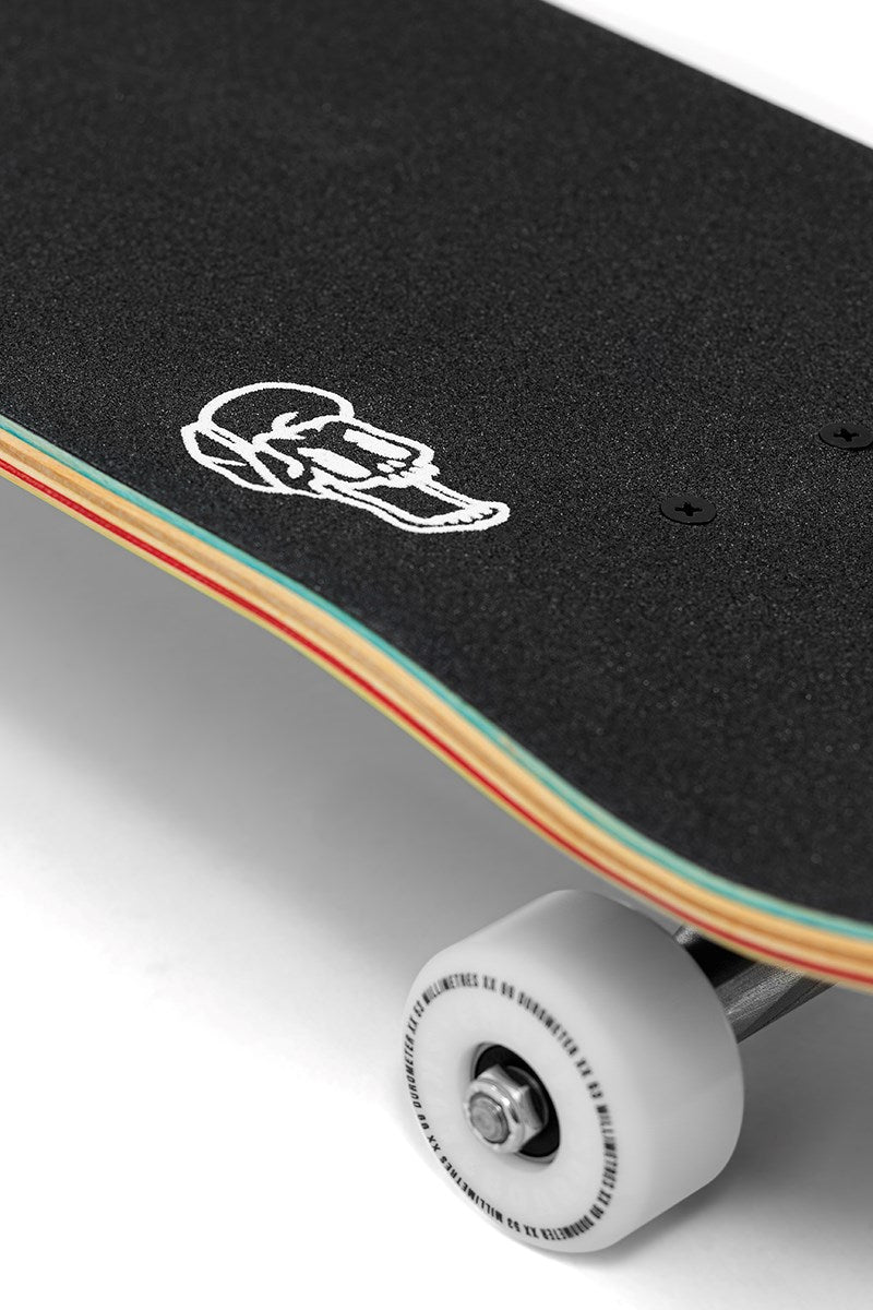 Close-up of the Enuff Yokai Dragon Complete Skateboard - 8.25" x 32.1", featuring black grip tape, a white skull graphic on a multicolored maple deck, and a white wheel with metal axle. Brand: Enuff.