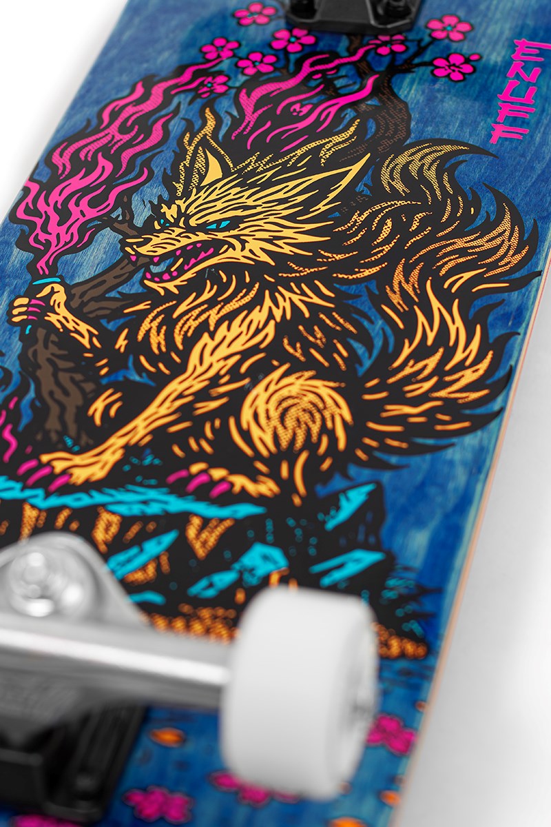 Close-up of the Enuff Yokai Kitsune Complete Skateboard (8.25" x 32.1") by Enuff, featuring a vibrant Japanese folklore-inspired fox with pink flowers, blue leaves, and bold orange-yellow fur on a blue wood deck; white wheels partly in view.