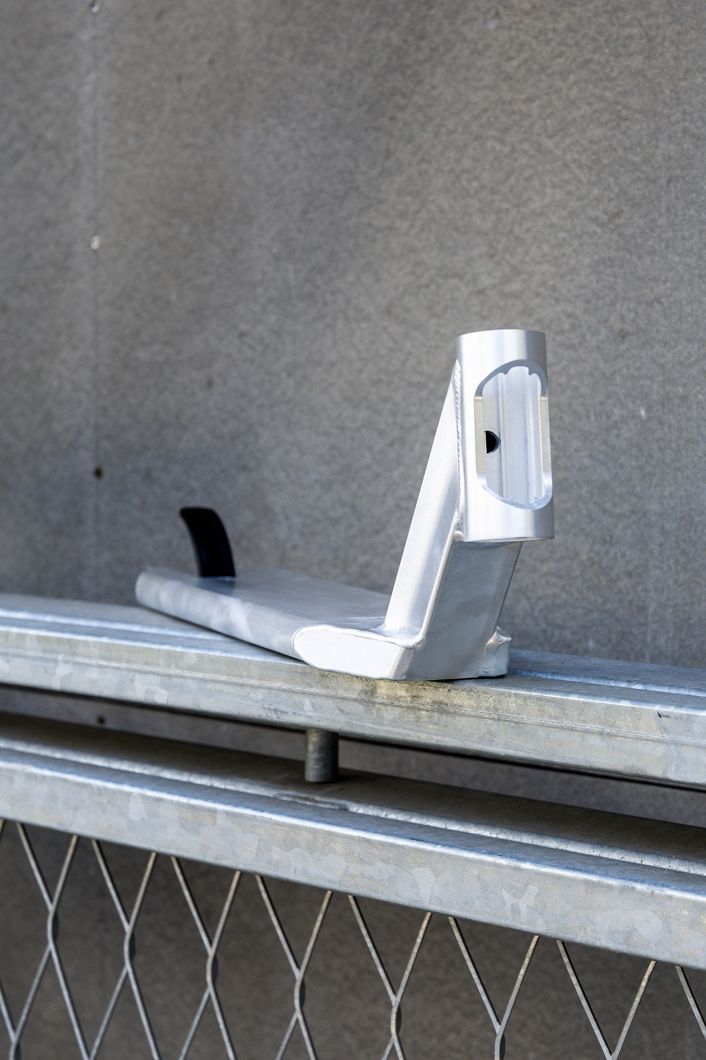 The Union Classic Pro Silver Stunt Scooter Deck - 4.75" by Union features a sturdy silver metal bracket with a curved base, upright section, black insert, and rectangular cutout, mounted on a galvanized bar against a gray wall.