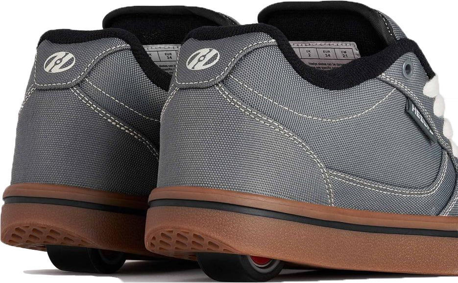 A close-up of the Heelys Pro 25 Boys Shoes in Grey, Antique White, and Black showcases their stylish gum soles and concealed wheels in the heels. Designed by Heelys, these sneakers provide both walking comfort and rolling fun with two wheels per shoe for added stability.