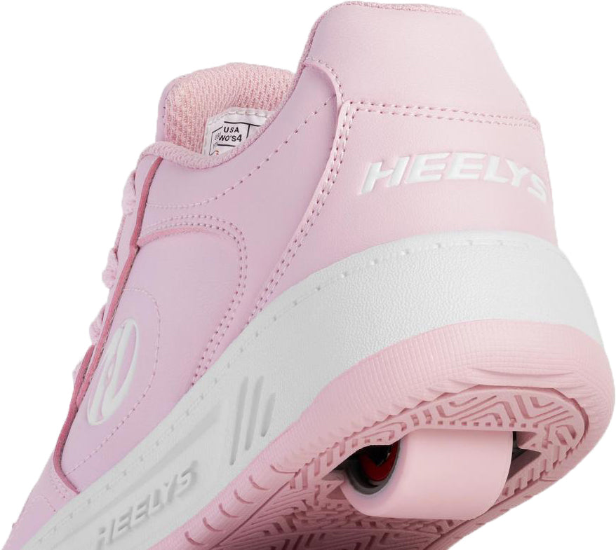Close-up view of the heel of a Heelys Gio Girls Shoes - Frost Pink / White, a light pink court-style sneaker with a single wheel embedded in the white rubber sole.