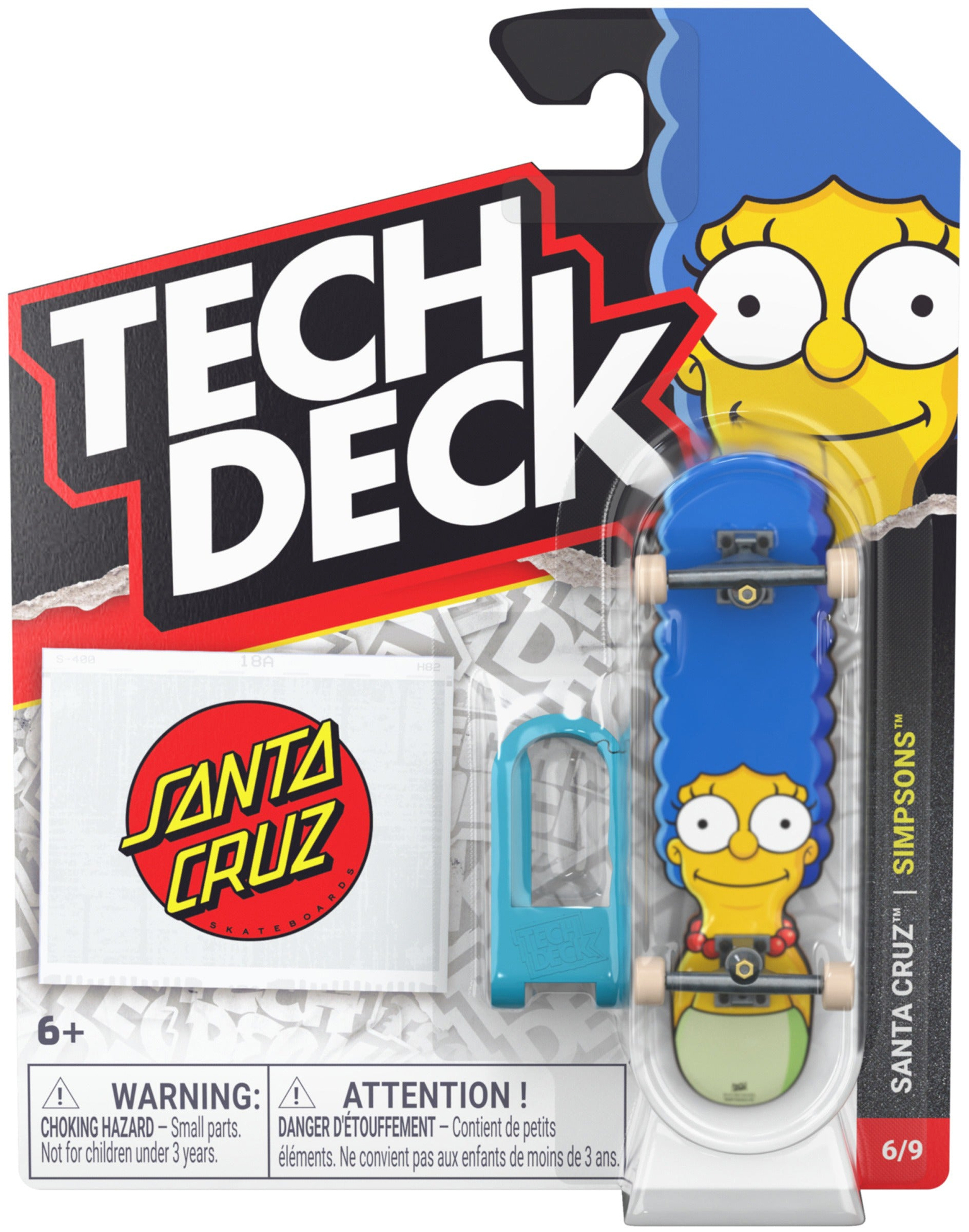The Tech Deck 96mm M04 Santa Cruz Fingerboard - Marge Simpson by Tech Deck features Marge Simpson’s face, includes a blue tool and a Santa Cruz Simpsons sticker, and comes in branded packaging displaying “Simpsons” and “6/9” in the bottom right corner along with a warning label.