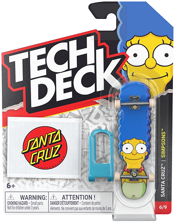 The Tech Deck 96mm M04 Santa Cruz Fingerboard - Marge Simpson by Tech Deck features Marge Simpson’s face, includes a blue tool and a Santa Cruz Simpsons sticker, and comes in branded packaging displaying “Simpsons” and “6/9” in the bottom right corner along with a warning label.