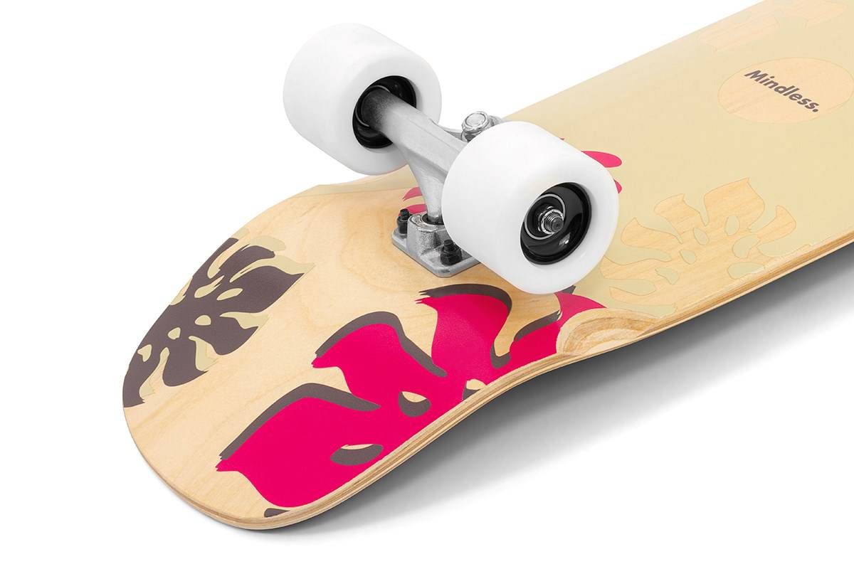 Close-up of the Mindless Oasis Cruiser Skateboard 32″ x 9″ - Natural featuring white wheels with ABEC 9 Chrome bearings, a metal truck, and a maple deck with pink and dark leaf patterns. “Mindless” is partially visible.