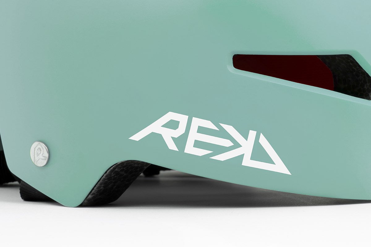 Close-up of the REKD Elite 2.0 Skate / Scooter Helmet in matte teal, featuring a white REKD logo, side vent, metal screw, and black padding—ideal protection for action sports.