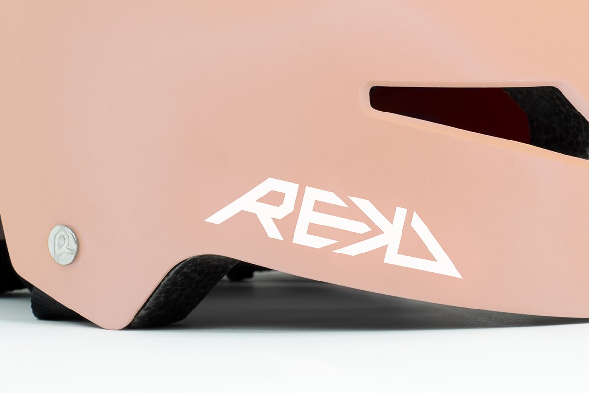 Close-up of the REKD Elite 2.0 Skate / Scooter Helmet in Peach / Purple, featuring a matte finish, stylized white REKD logo on the side, top vent, and a small round silver rivet on the left edge.