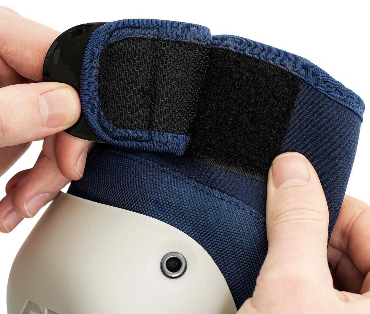 Close-up of hands fastening the black Velcro strap on a blue and white knee pad from the REKD Shield Triple Skate Protection Pad Set by REKD, designed for action sport protection.