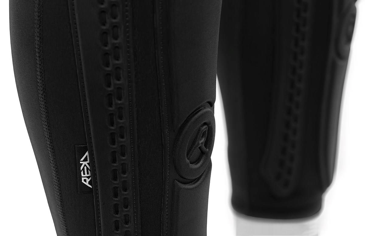 Close-up of REKD Energy Covert Long Shin Skate Protection Guards - Black, featuring a textured vertical strip and a circular logo patch.