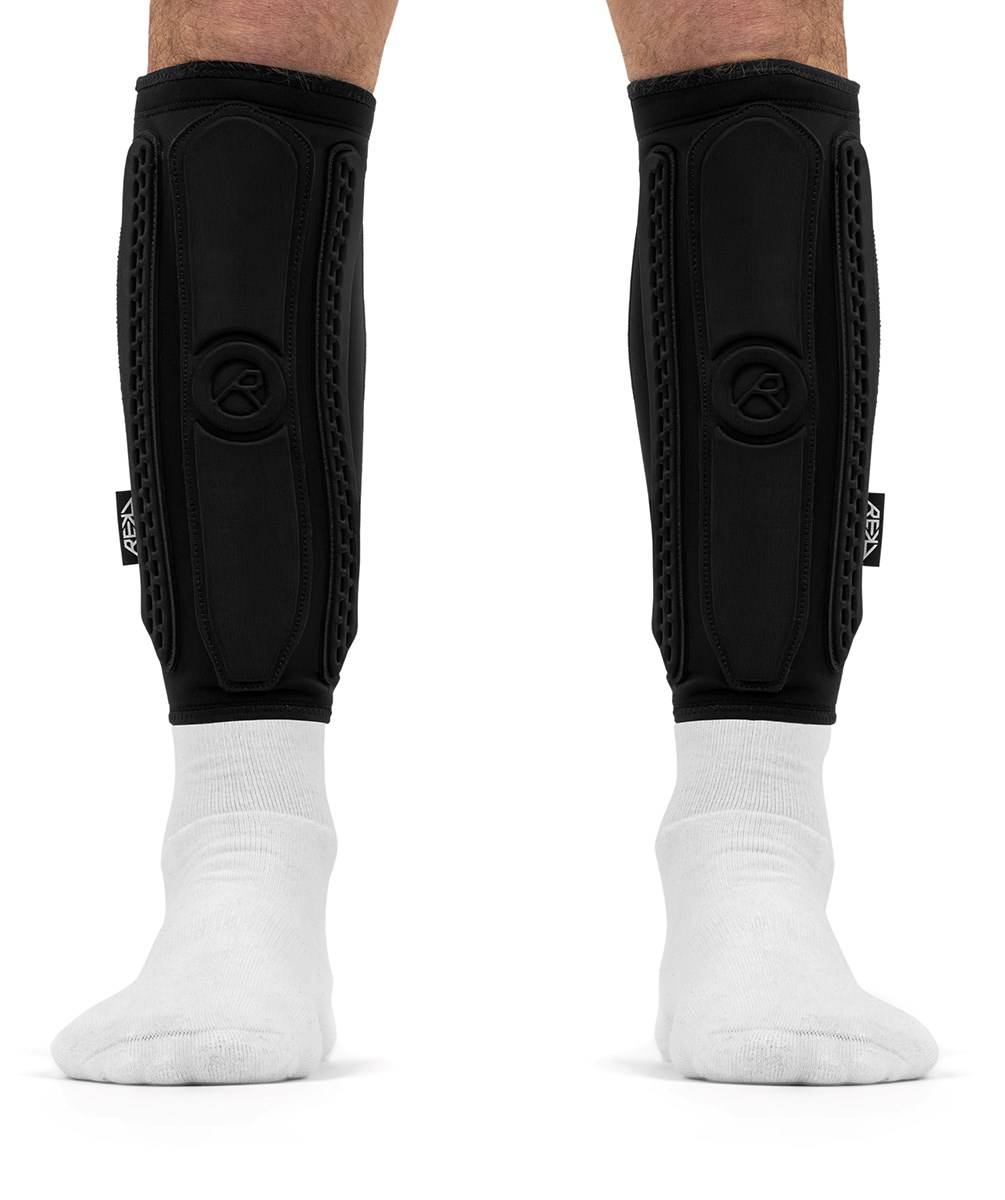 A pair of slim black REKD Energy Covert Long Shin Skate Protection Guards worn over white socks.