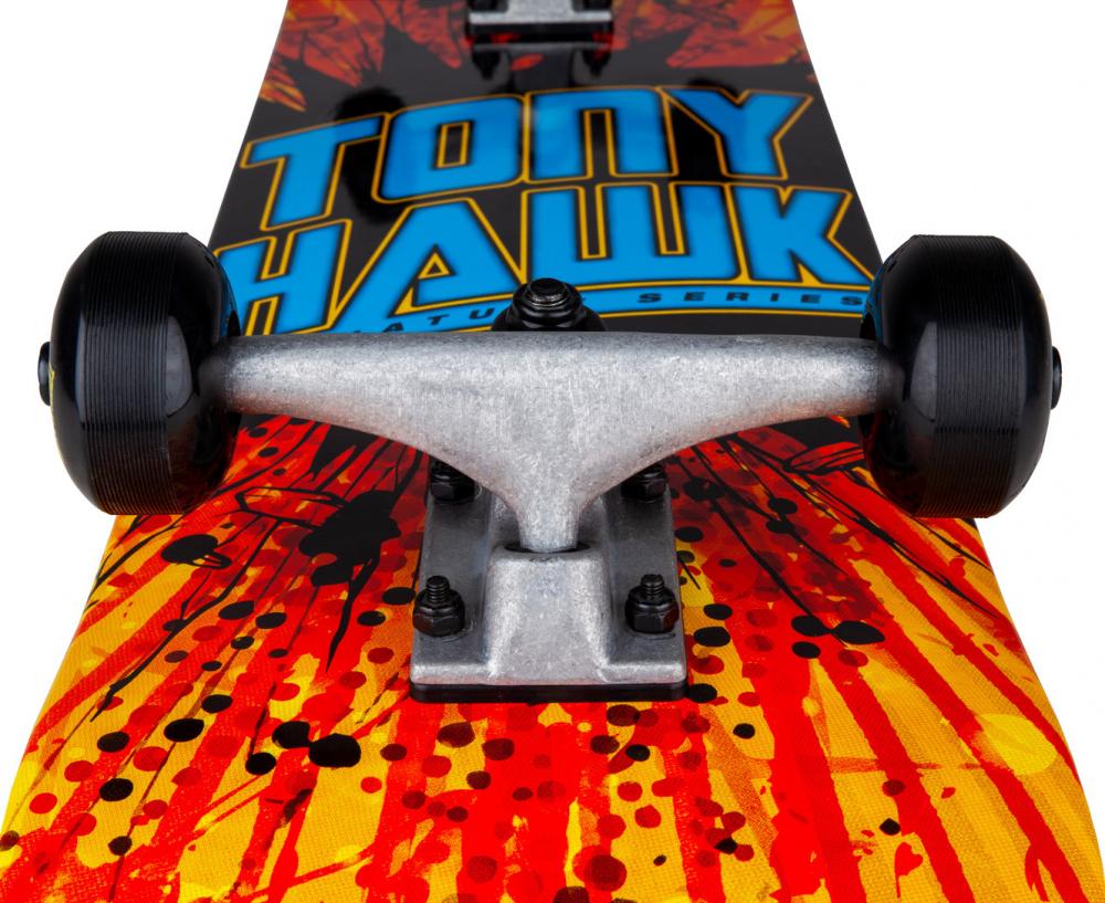 Close-up of the Tony Hawk SS 180 Series Shatter Logo Complete Skateboard—featuring bold blue “Tony Hawk” text and a vivid red-and-yellow shatter design on its 7.75″ x 31″ maple deck—showing off the front trucks and black wheels; perfect as a beginner complete skateboard.
