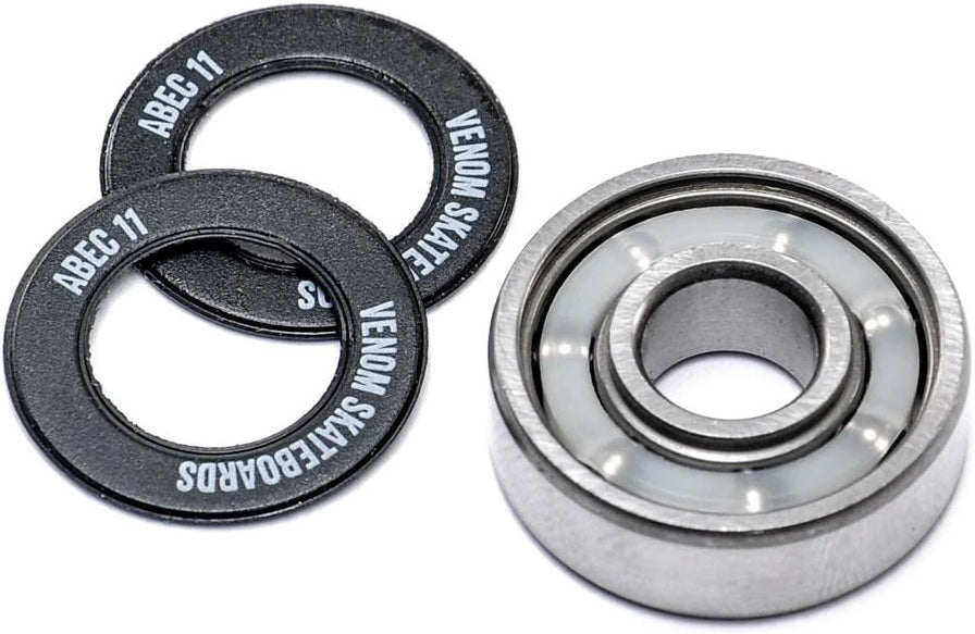 A skateboard bearing next to two black rubber bearing shields printed with “ABEC 11” and “Venom Skateboards” for Venom ABEC 11 Skateboard Bearings - 8 Pack.