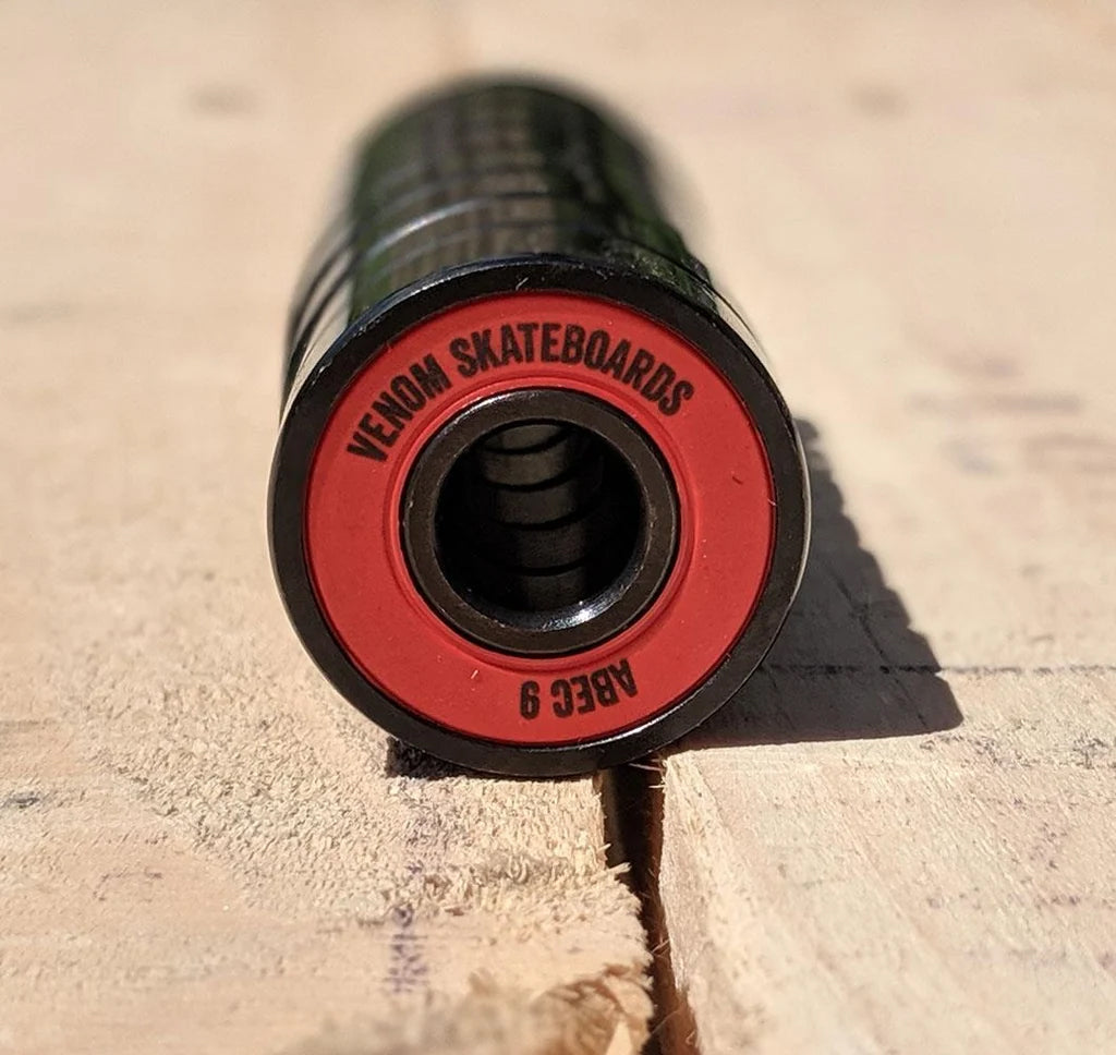 Close-up of a cylindrical Venom ABEC 9 Skateboard Bearings - 8 Pack with a red rim printed with the text “VENOM SKATEBOARDS” and “ABEC 9”.